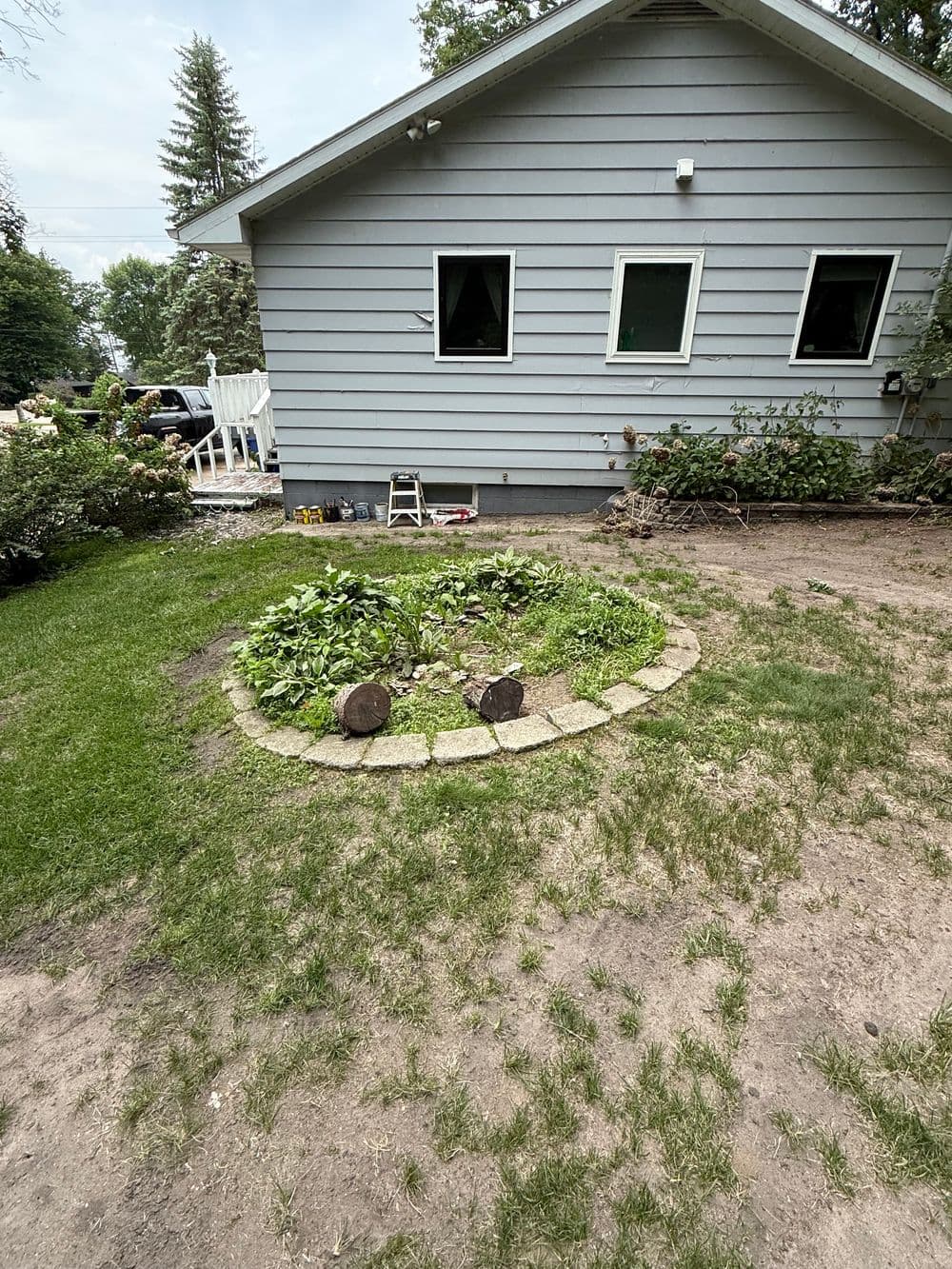 Garden landscape with round stone border, greenery, and a house in the background.