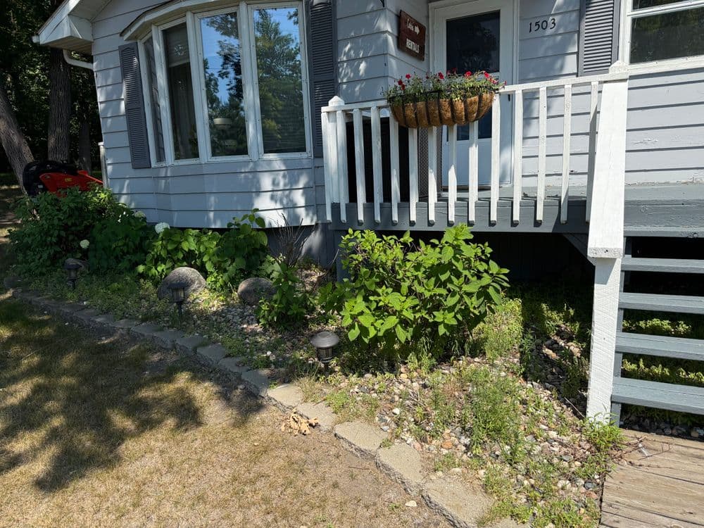Front of a house with a flower basket, greenery, path, and outdoor lighting fixtures.