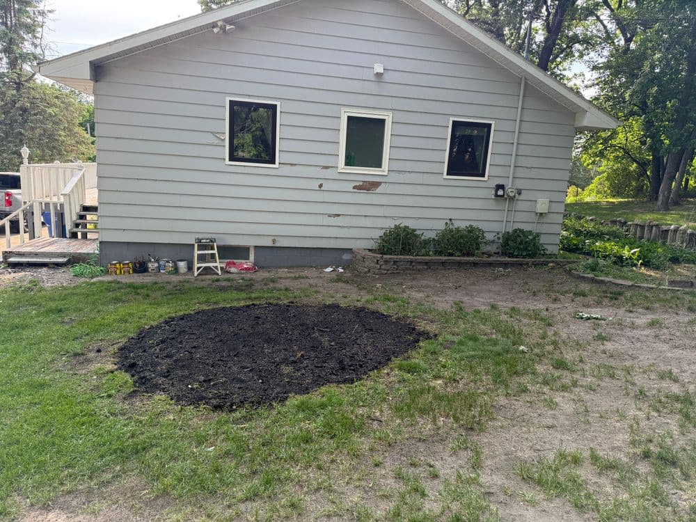Excavated patch of soil next to a gray house for landscaping or gardening project.